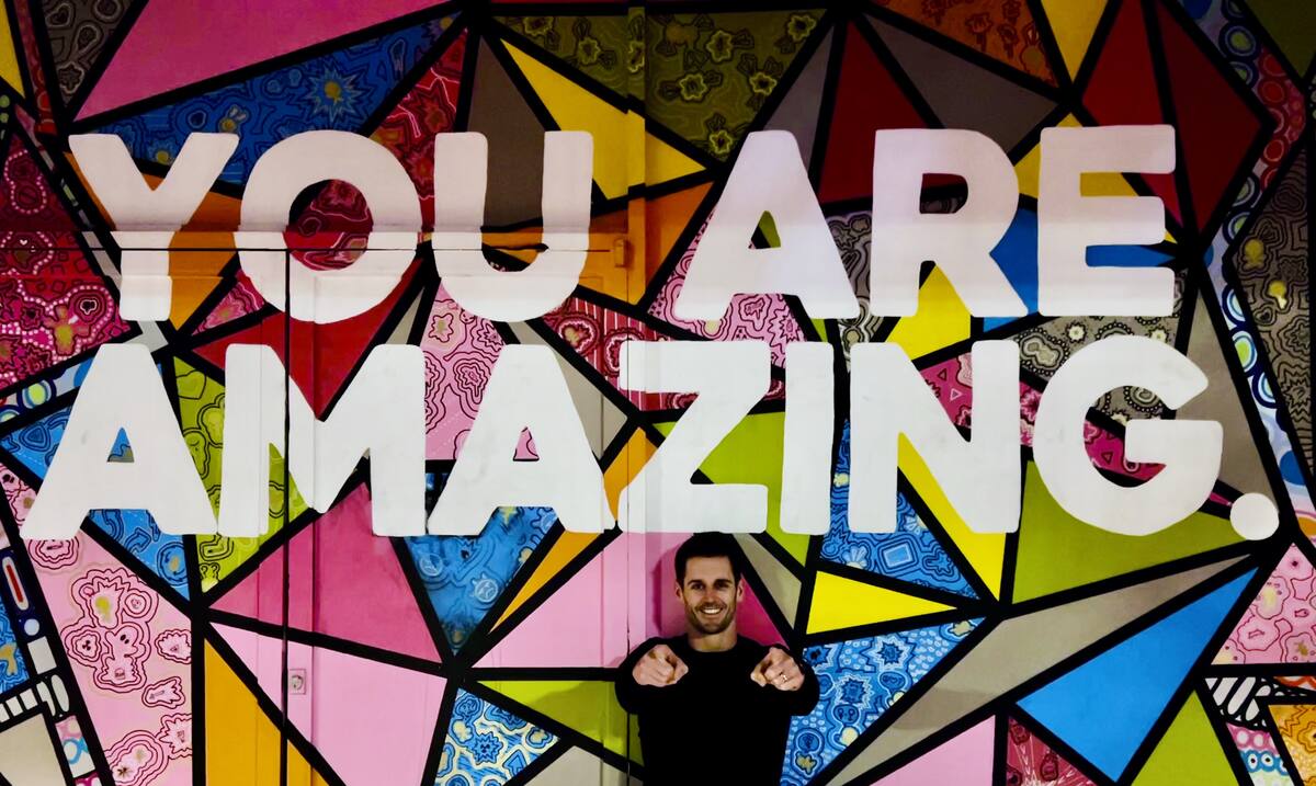 Ben Miller pointing at the camera in front of a colorful mural that reads 'You are amazing.'